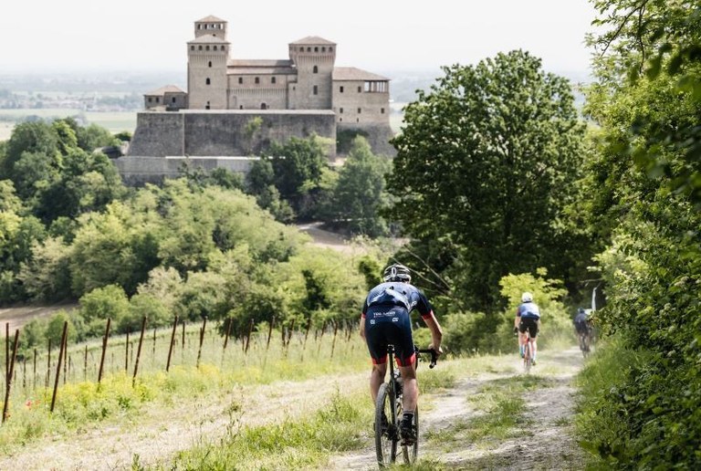 Ciclisti su terreno sterrato con Castello di Torrechiara in sfondo, ph. Giacomo Podetti 