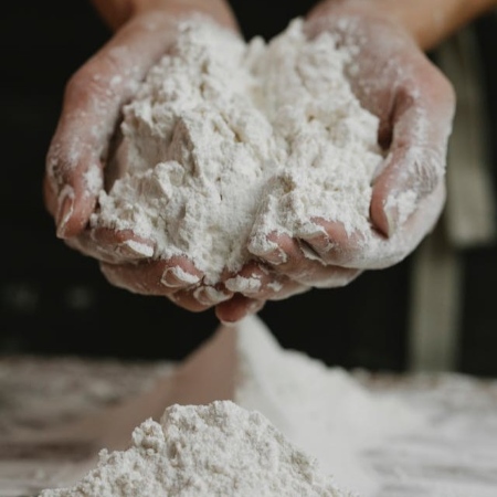 Due mani raccolgono farina di grano da un cumulo su un piano di lavoro (Fonte Klaus Nielsenda Pexels)