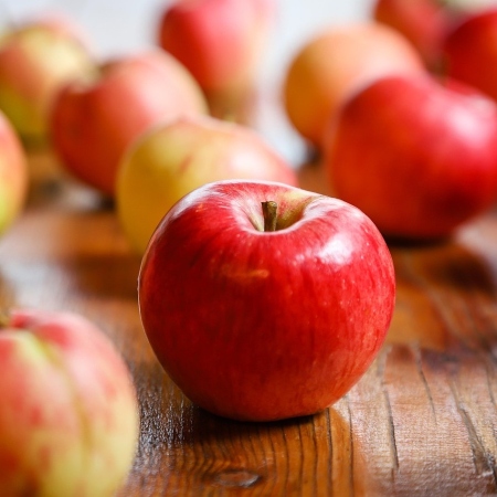Mela rossa in primo piano su tavolo di legno, con altre mele sfocate sullo sfondo (Fonte Alfons Landsmann da Pixabay)