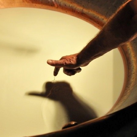 Mano che esegue la prova della coagulazione sollevando un sottile filamento di cagliata dalla superficie del latte in una grande caldaia di rame durante la lavorazione del Parmigiano Reggiano (Fonte Fabrizio Dell’Aquila)