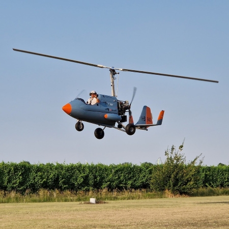 Minicottero leggero impiegato per il monitoraggio dei vigneti, ripreso in volo a bassa quota con un operatore in cabina sopra un’area erbosa, con filari di vigneto sullo sfondo (Foto RER)